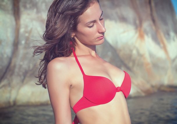 Mujer joven retrato al aire libre en la costa rocosa salvaje playa piedra paisaje vista al mar en traje de baño bikini rojo
 - Foto, imagen