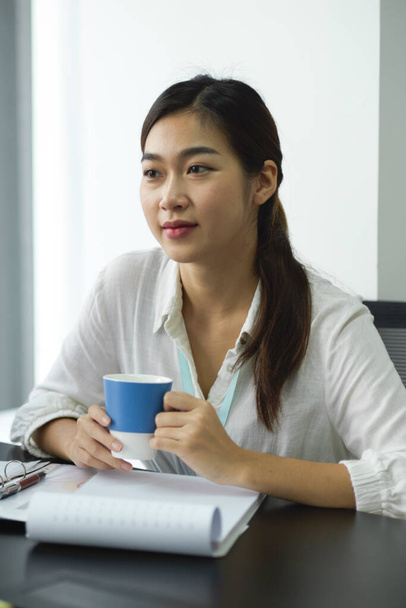 Hermosa empleada de negocios sosteniendo una taza de café mientras está sentada en una sala de reuniones. primer plano - Foto, Imagen