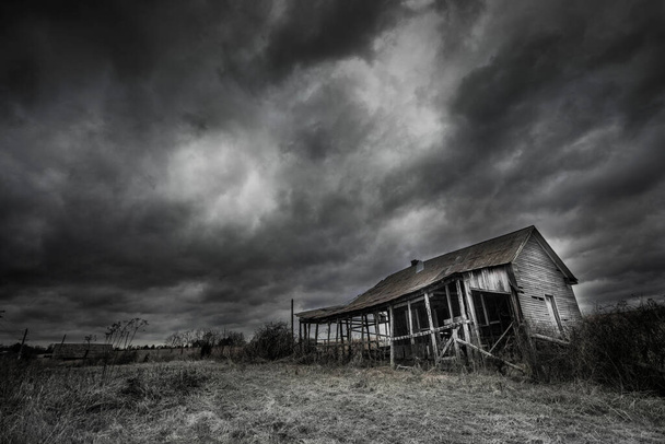 Ένα εγκαταλελειμμένο σπίτι με σκοτεινό δραματικό συννεφιασμένο ουρανό - Φωτογραφία, εικόνα