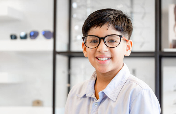 Optik mağazasından gözlük seçen gülümseyen Hintli-Taylandlı çocuk, optik mağazada gözlük takan melez ırkın portresi - Fotoğraf, Görsel