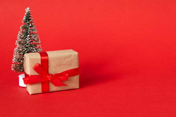 Kırmızı kurdeleli hediye kutusu ve kırmızı arka planda köknar ağacı. Noel hediyesi, yeni yıl, sevgililer günü - Fotoğraf, Görsel