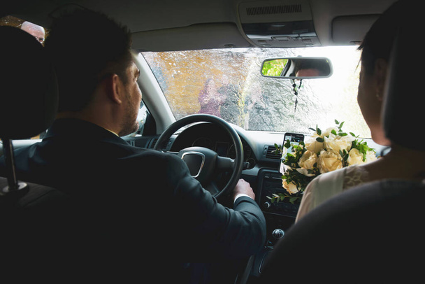 Interior front seat view bride and groom sit in car while friends spray sparkling wine on car . Culture and wedding celebrations in Lithuania - 写真・画像
