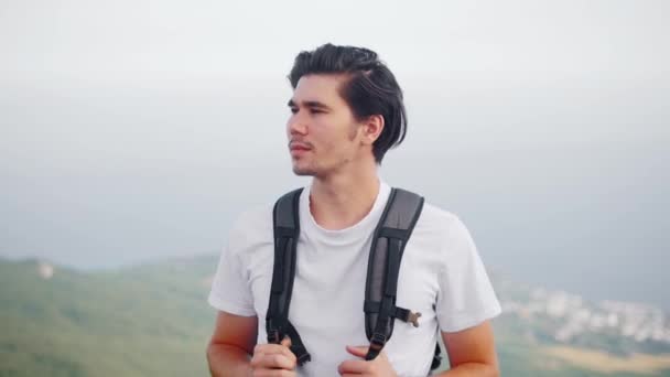 Поездка - молодой человек-турист стоит на вершине горы и оглядывается по сторонам - Кадры, видео