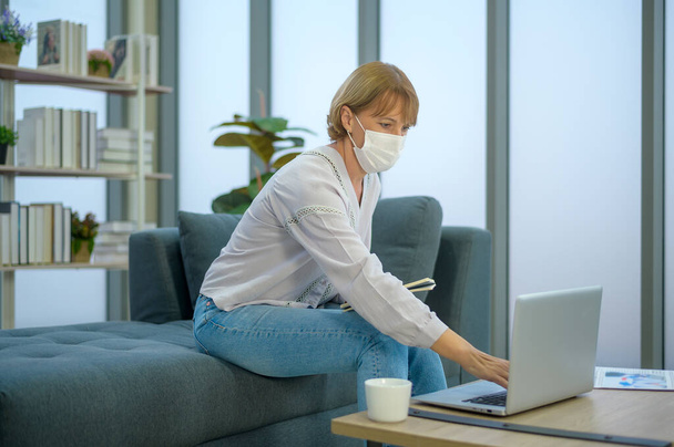 A caucasian senior Businesswoman with mask is working in modern office - Photo, image