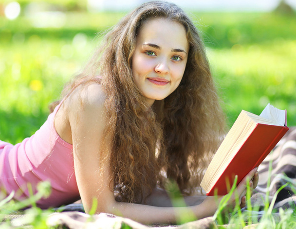 Portrait young happy girl reading a book lying in a park in sunn - Foto, Imagem