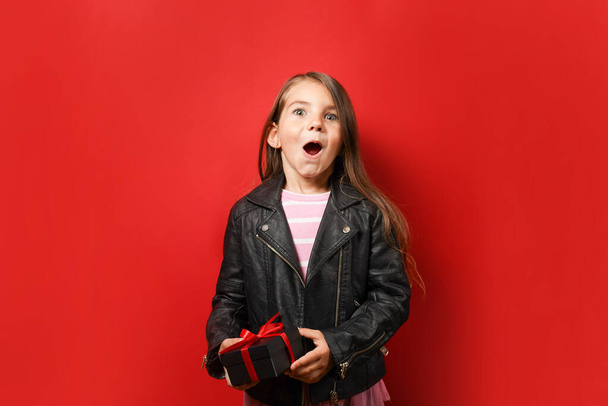 Zaskoczony dziewczynka trzyma czarne pudełko na czerwonym tle z miejsca na ksero. Koncepcja Black Friday - Zdjęcie, obraz