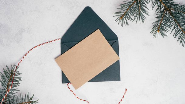 白いコンクリートの背景に緑のオープン封筒クリスマスツリーの枝と空白のクラフト紙のグリーティングカード。未接続のコードで新年の封筒.コピースペース。トップ表示 - 写真・画像