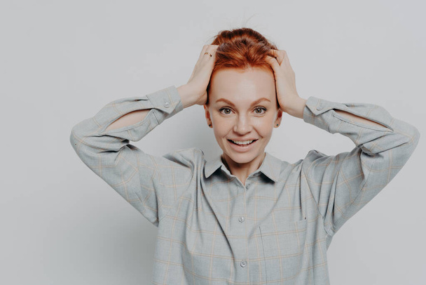 Excited amazed redhaired woman holding head in hands and looking at camera with surprised expression - Photo, Image