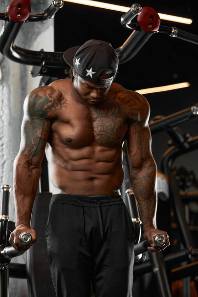 強く、筋肉の暗い肌の男はジムで近代的な機器に訓練します。筋肉ポンプフィットネストレーナーの肖像 - 写真・画像