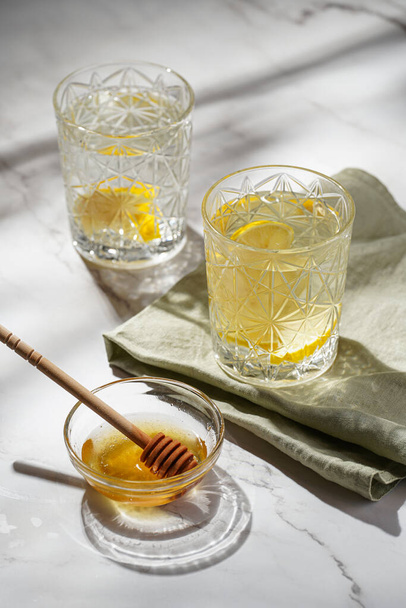 Two glasses with water and lemon, honey in the morning light - breakfast - Photo, Image