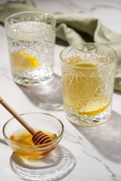 Two glasses with water and lemon, honey in the morning light - breakfast - Fotó, kép
