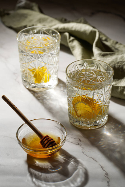 Two glasses with water and lemon, honey in the morning light - breakfast - Фото, изображение