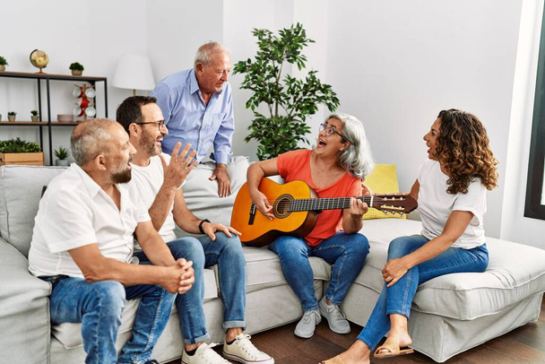 Grupo de amigos de meia-idade fazendo festa tocando guitarra clássica sentado no sofá em casa. - Foto, Imagem