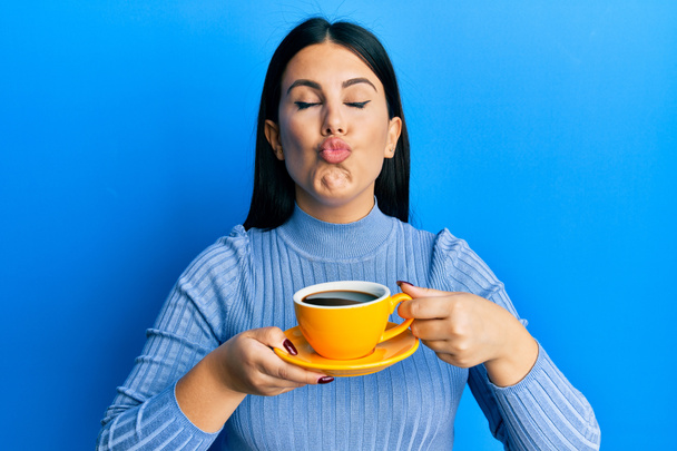 Beautiful brunette woman drinking a yellow cup of black coffee looking at the camera blowing a kiss being lovely and sexy. love expression.  - Фото, зображення