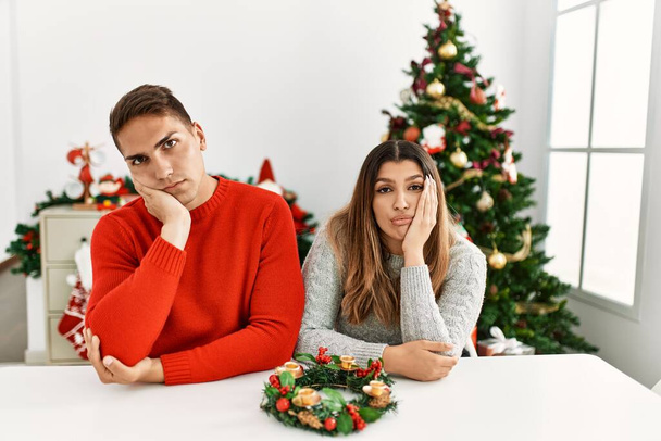 Jovem casal hispânico sentado à mesa no Natal pensando que parece cansado e entediado com problemas de depressão com os braços cruzados.  - Foto, Imagem