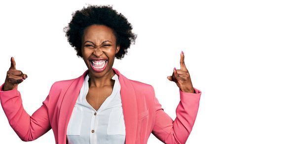 African american woman with afro hair wearing business jacket shouting with crazy expression doing rock symbol with hands up. music star. heavy music concept.  - Photo, Image