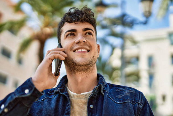 Mladý hispánec se šťastně usmívá a mluví po telefonu ve městě - Fotografie, Obrázek