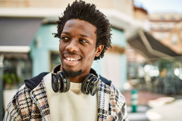 Schöner schwarzer Mann mit Afro-Haaren, der Kopfhörer trägt und im Freien glücklich lächelt - Foto, Bild