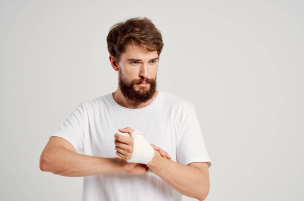 male patient in a white T-shirt with a bandaged hand posing isolated background - Foto, afbeelding