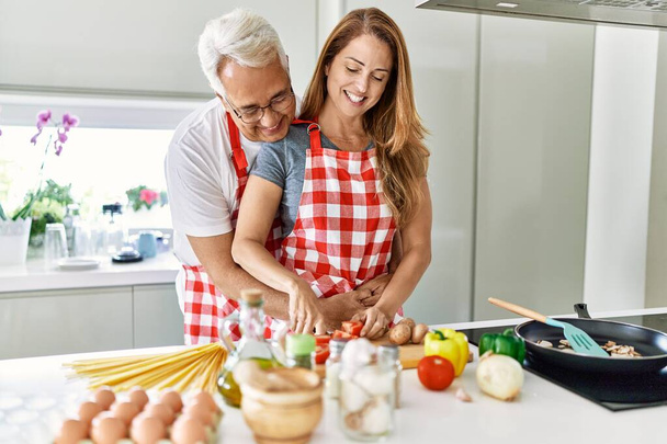 Испанская пара средних лет улыбается счастливой и обнимает кухню. - Фото, изображение