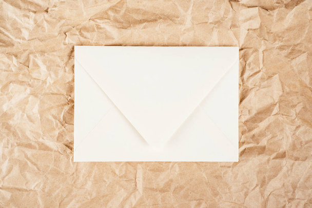 Background image of rough crumpled recycled textured kraft paper with white cardboard envelope in middle. Top view. Copy space - Photo, Image