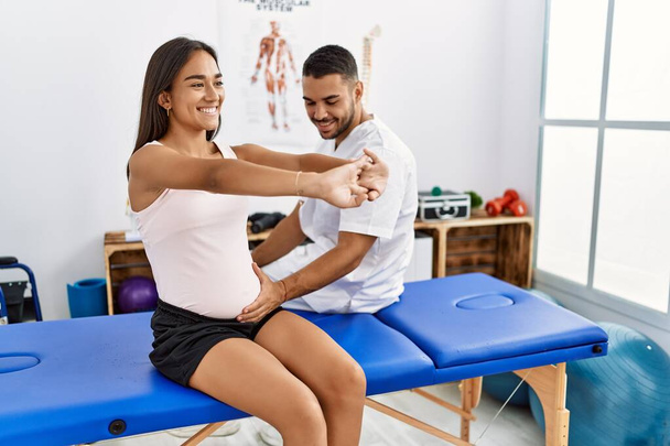 Latin man and woman wearing physiotherapist uniform having pregnancy rehab session at physiotherapy clinic - Photo, Image