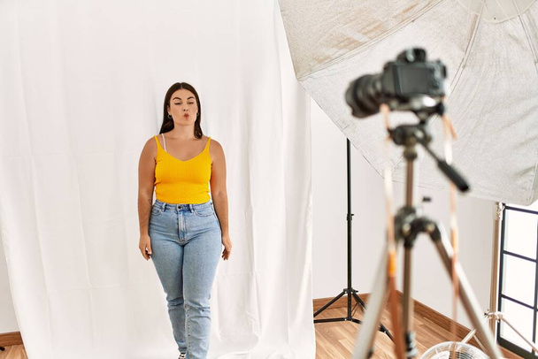 Young beautiful hispanic woman posing as model at photography studio making fish face with lips, crazy and comical gesture. funny expression.  - Foto, imagen