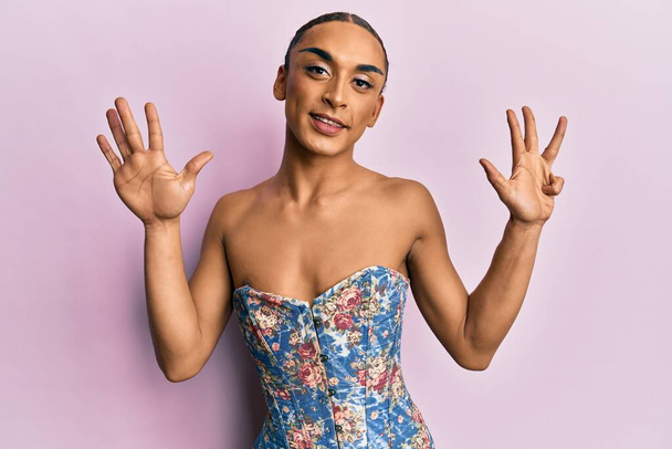 Hispanic man wearing make up and long hair wearing elegant corset showing and pointing up with fingers number nine while smiling confident and happy.  - Foto, Imagen