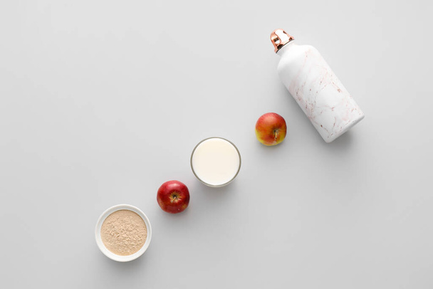 Glass of protein shake, bowl with powder, bottle and apples on light background - 写真・画像