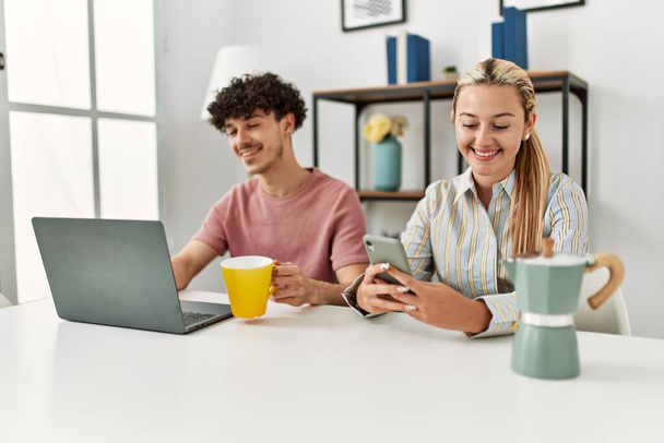 Молодая пара, использующая ноутбук и смартфон, пьет кофе дома. - Фото, изображение