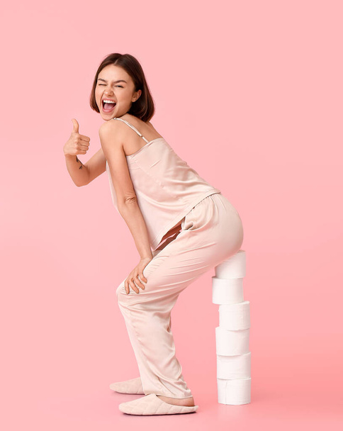 Young woman with many rolls of toilet paper showing thumb-up on color background - Fotografie, Obrázek
