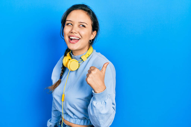 Nuori latino tyttö kuuntelee musiikkia kuulokkeilla osoittaa peukalo ylös puolella hymyillen onnellinen suu auki  - Valokuva, kuva