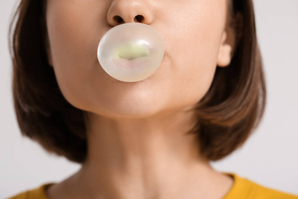 Young woman with chewing gum on light background, closeup - Foto, Imagen
