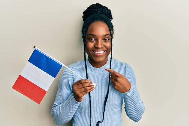Afričanky americká žena s spletené vlasy drží francouzskou vlajku s úsměvem šťastný ukazující rukou a prstem  - Fotografie, Obrázek