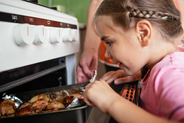 Granny and small girl take pan with baked roast chicken and potato out of oven, together in kitchen - Photo, image