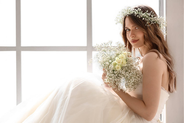 Beautiful bride with bouquet of flowers sitting on window sill - 写真・画像
