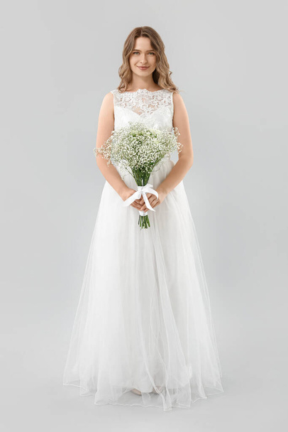 Beautiful bride with bouquet of flowers on light background - Valokuva, kuva