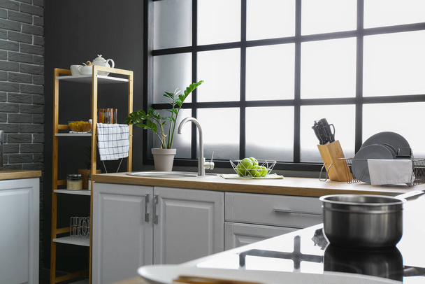 Ezüst mosogató, virágcserép és tál almával a konyhaasztalon ablak mellett - Fotó, kép