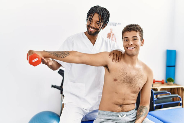 İki erkek fizyoterapist ve hasta klinikte halter kullanarak rehabilitasyon seansı yapıyorlar. - Fotoğraf, Görsel