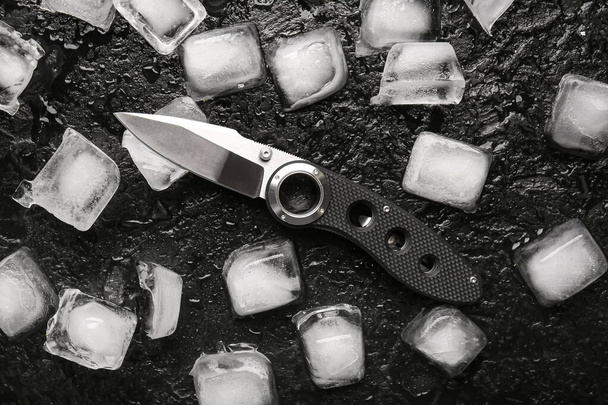 Összehajtható zsebkés gumírozott fogantyú és jégkockák fekete texturált háttér - Fotó, kép