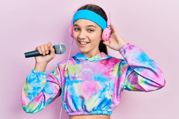 Young brunette girl singing song using microphone wearing sportswear celebrating crazy and amazed for success with open eyes screaming excited.  - Foto, afbeelding