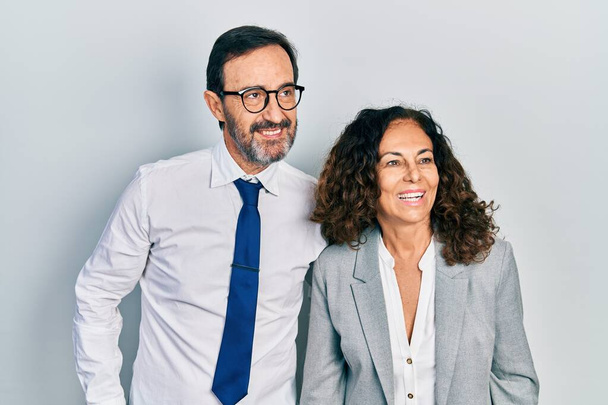 Middle age couple of hispanic woman and man wearing business office uniform looking away to side with smile on face, natural expression. laughing confident.  - Photo, Image