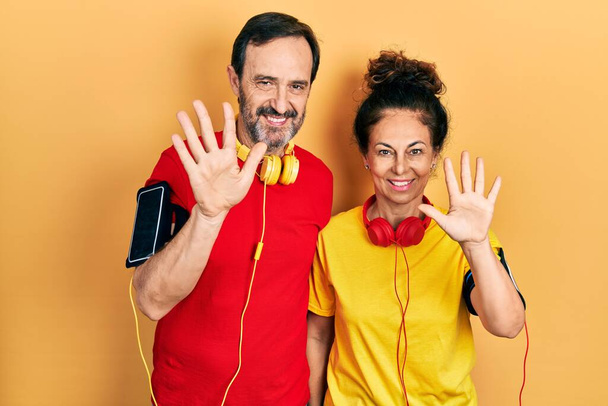 Para Hiszpanek w średnim wieku, ubrana w strój sportowy i opaskę wskazującą palcem numer dziesięć, uśmiechająca się pewna siebie i szczęśliwa..  - Zdjęcie, obraz