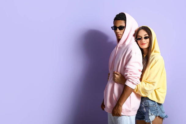 Elegante pareja joven en sudaderas con capucha sobre fondo violeta - Foto, imagen