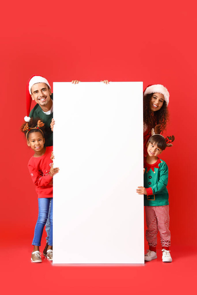 Happy family in Christmas clothes with blank poster on red background - Foto, Imagem