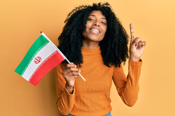 アフロヘアのアフリカ系アメリカ人女性は、幸せな顔をしたアイデアや質問を指差す指で笑顔Kurdistanフラグを保持します,ナンバーワン  - 写真・画像
