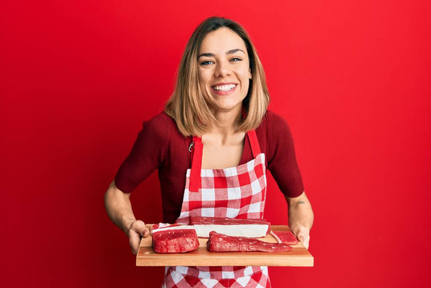 Young caucasian blonde woman holding board with raw meat smiling and laughing hard out loud because funny crazy joke.  - Photo, Image