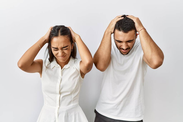 Young interracial couple standing together in love over isolated background suffering from headache desperate and stressed because pain and migraine. hands on head.  - Photo, Image