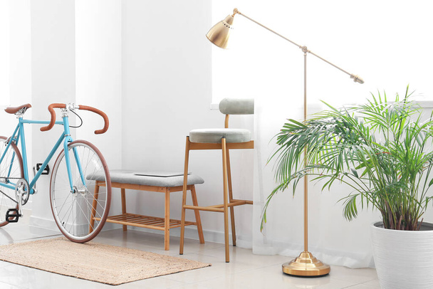 Интерьер светлой комнаты со стулом, оттоманом, лампой и велосипедом - Фото, изображение