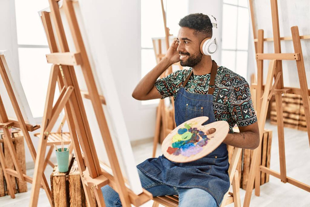 Jeune artiste afro-américain souriant heureux d'écouter de la musique et de la peinture au studio d'art. - Photo, image